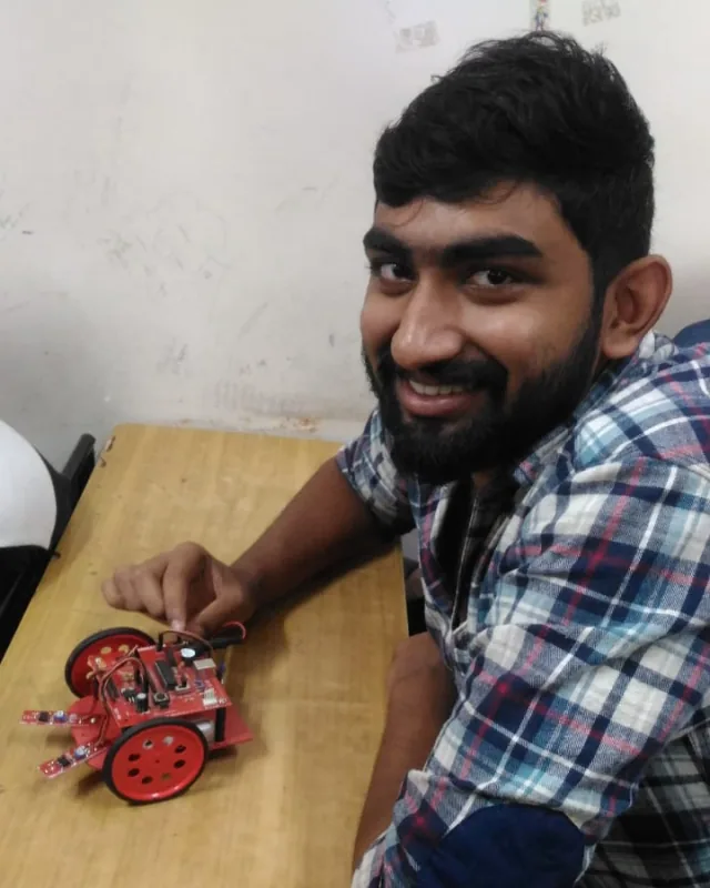 Sumit Gundawar at a workbench with the line-following robot: a red chassis on two wheels, with a pair of infrared sensor arms reaching out in front of it.